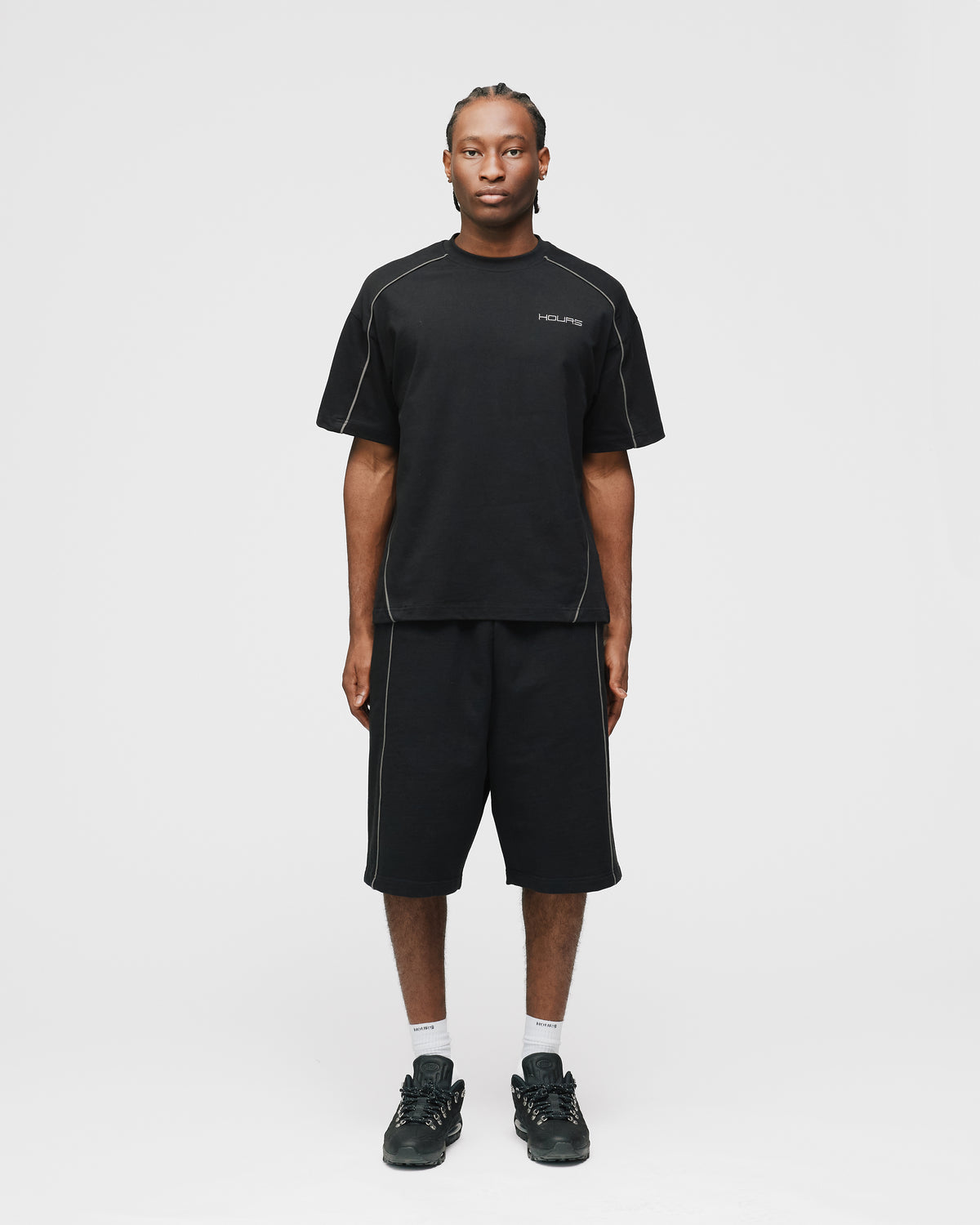 Person wearing a black t-shirt and shorts set with 'Hours' branding on a white background